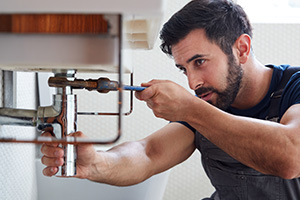 Ein junger Handwerker befestigt einen Waschbecken-Abfluss in einem Badezimmer. 