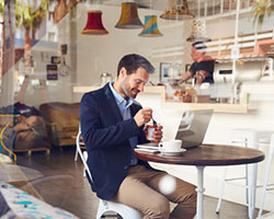 Ein Mann sitzt im Bistro, arbeitet am PC und isst.