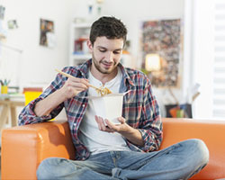 Ein Mann sitzt in seiner Wohnung auf der Couch und isst.