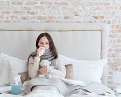 Eine unglückliche, kranke Frau sitzt mit Schal im Bett.