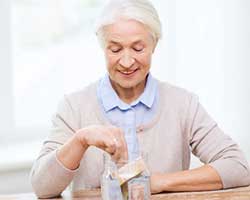 Eine Seniorin legt Geld in ein großes Glas voll mit Geldscheinen.