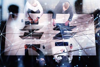 Vier Geschäftsmänner sitzen sich an Schreibtischen gegenüber und arbeiten an Computern. Ein digitales Netzwerk spannt sich über das Bild.