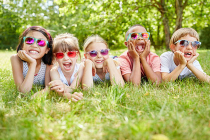 Ein Kinderspiel: Kinderbetreuungskosten richtig absetzen Fünf Kinder mit Sonnenbrillen liegen auf einer Wiese, sie stützen sich auf Ihre Hände auf und lachen fröhlich in die Kamera.