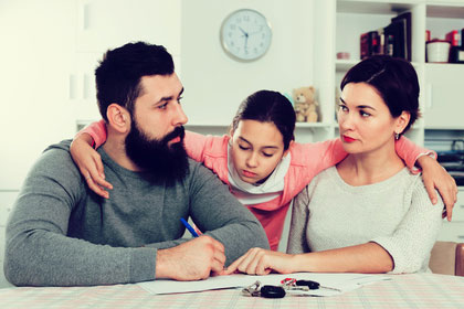 Eltern, ihr Betreuungsanteil und der Freibetrag Ein Kind klammert sich zwischen seine Eltern, die sich anschauen. Der Vater hat einen Stift in der Hand, die Mutter zeigt mit dem Finger auf Papiere, die auf einem Tisch liegen.