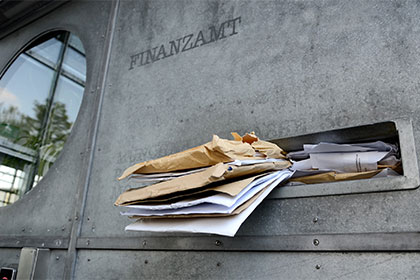 Antragsveranlagung: Frist für das Steuerjahr 2015 läuft ab Auf einer steinernen Hauswand steht die Aufschrift Finanzamt. Darunter befindet sich ein Briefkastenschlitz, aus dem viele Briefumschläge herausquellen. Links neben der Aufschrift befindet sich ein rundes Fenster.