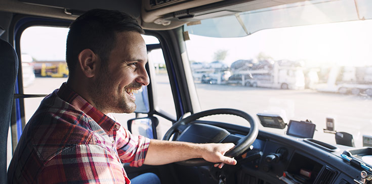 Neuer Pauschbetrag für LKW-Fahrer ab 2020 Ein Mann in kariertem Hemd sitzt am Lenkrad eines großen LKW. Er schaut aus der Frontscheibe heraus und lächelt.