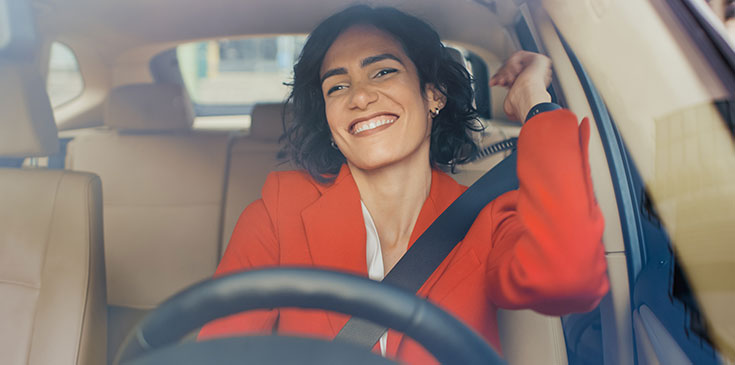 Eine Frau mit rotem Oberteil sitzt lächelnd in ihrem Auto.