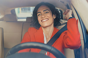 Eine Frau mit rotem Oberteil sitzt lächelnd in ihrem Auto.