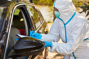 Eine Person in Schutzanzug steht am Autofenster und nimmt die persönlichen Daten auf.