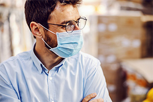 Ein Mann in Hemd schaut nach rechts. Er trägt eine Brille und eine Maske.