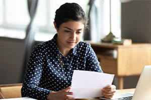Eine Frau sitzt am Schreibtisch und blickt auf einen Papierbogen.