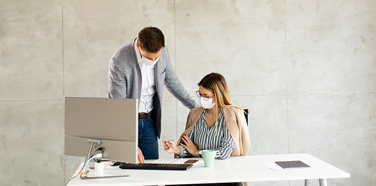 Viertes Corona-Steuerhilfegesetz: Homeoffice, Pflege-Bonus, Fristverlängerung und mehr Eine Frau sitzt am Arbeitsplatz. Ihr Kollege schaut ihr über die Schulter und sie besprechen Unterlagen.
