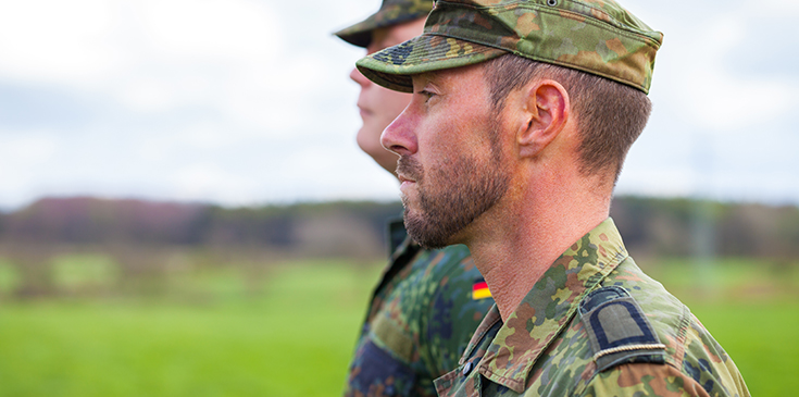 Zwei Soldaten in Tarnuniform stehen nebeneinander und blicken geradeaus.