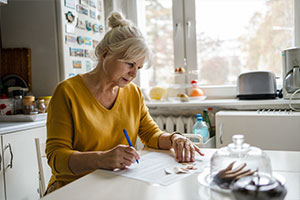 Eine Dame sitzt an ihrem Küchentisch, hat Dokumente sowie Bargeld vor sich und füllt ihren Freistellungsauftrag aus.