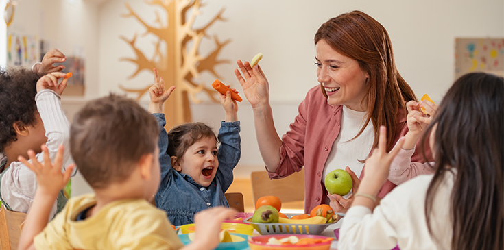 Kann ich die Ferienbetreuung meines Kindes von der Steuer absetzen? Fröhliche Erzieherin betreut Kinder in einer Kindertagesstätte – Kinderbetreuungskosten steuerlich absetzen mit Tipps vom Steuerring.