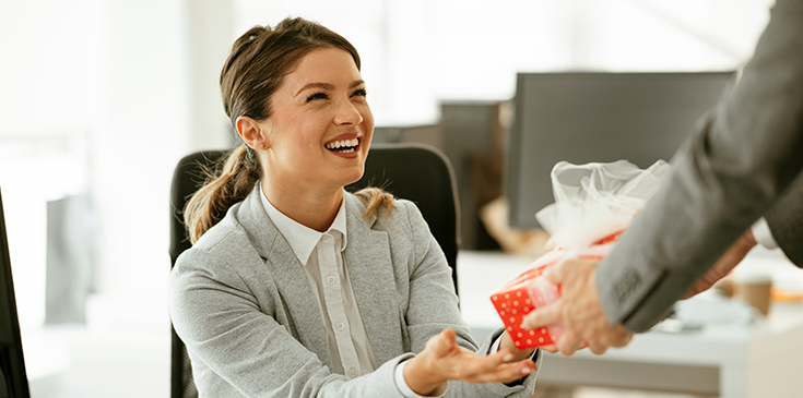 Steuerfreie Arbeitgeberzuschüsse: So profitieren Arbeitnehmer Junger Geschäftsmann überrascht seine Kollegin im Büro mit einem Geschenk.