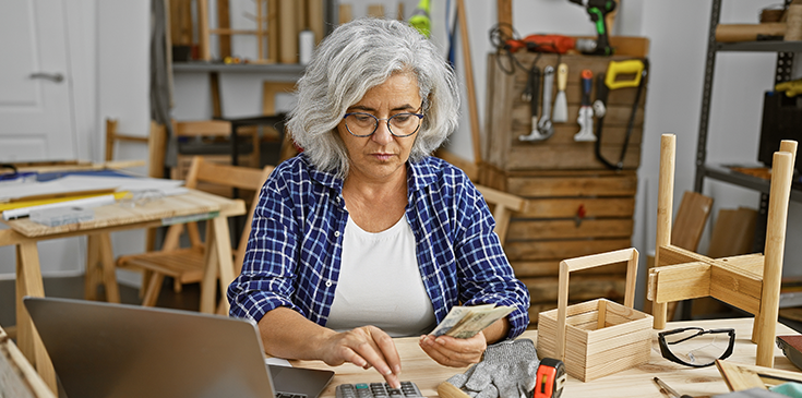 Eine Frau sitzt am Schreibtisch und berechnet, wann es sinnvoll ist ihre Handwerkerkosten zu begleichen. 