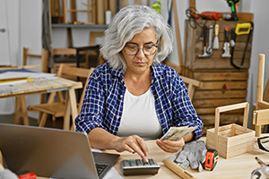 Eine Frau sitzt am Schreibtisch und berechnet, wann es sinnvoll ist ihre Handwerkerkosten zu begleichen. 