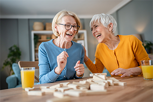 Zwei ältere Frauen lachen gemeinsam beim Spielen eines Gesellschaftsspiels an einem Tisch.