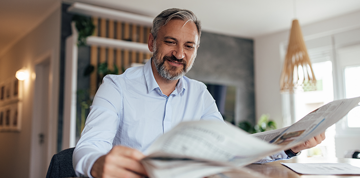 Ein Mann sitzt an Küchentisch und liest in einer Zeitung.