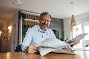 Ein Mann sitzt an Küchentisch und liest in einer Zeitung.