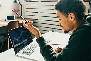 Ein Mann arbeitet remote am Laptop und analysiert Aktien- und Kryptowährungsmärkte.