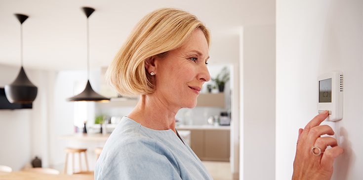 Nahaufnahme einer Frau, die zu Hause am Thermostat die Temperatur der Zentralheizung einstellt.