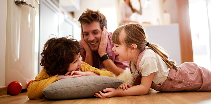 Familie mit zwei Kindern beim Spielen auf dem Wohnzimmerboden – symbolisch für die Auswirkungen von möglichen Steueränderungen zum Beispiel auf Familien.