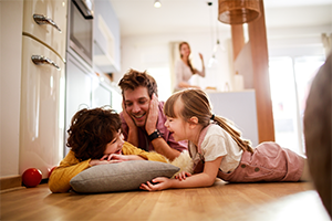 Familie mit zwei Kindern beim Spielen auf dem Wohnzimmerboden – symbolisch für die Auswirkungen von möglichen Steueränderungen zum Beispiel auf Familien.