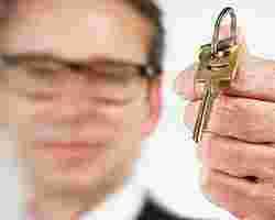 Ein Mann hält einen Hausschlüssel zu Übergabe hin.