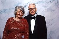 Walter Dieckmann und seine Frau Irene. Eine Frau in Abendkleid und ein Mann in Anzug und Fliege stehen vor einem steinigen Hintergrund. Sie lächeln in die Kamera.