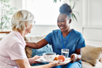 Eine jüngere Frau bringt einer älteren Dame Essen vorbei.