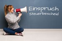 Für wen gilt die einmonatige Einspruchsfrist beim Steuerbescheid? Eine junge Frau in Rollkragenpullover, Jeans und Chucks sitzt im Schneiderschnitz vor einer Wand. Sie ist zur Seite gedreht und hält ein Megafon in der Hand, in das sie reinspricht. An der Wand erscheint, quasi aus dem Megafon heraus, der Schriftzug „Einspruch Steuerbescheid“
