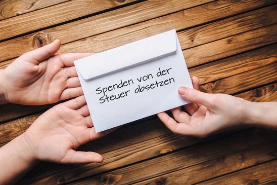 Spenden von der Steuer absetzen Rechts im Bild reicht eine Hand einen Briefumschlag mit der Aufschrift „Spenden von der Steuer absetzen“ an zwei Hände links im Bild weiter. Diese Hände sind offen gehalten, sodass der Umschlag leicht abgelegt werden kann.