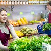 Eine junge Frau mit braunen Haaren räumt die Gemüseregale im Supermarkt ein.