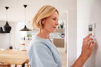 Nahaufnahme einer Frau, die zu Hause am Thermostat die Temperatur der Zentralheizung einstellt.