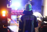 Steuerfrei für ehrenamtliche Helfer Ein Mann mit Helm und Feuerwehruniform ist von hinten zu sehen. Links neben ihm und verschwommen im Hintergrund sind Feuerwehrautos zu erkennen.