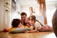 Familie mit zwei Kindern beim Spielen auf dem Wohnzimmerboden – symbolisch für die Auswirkungen von möglichen Steueränderungen zum Beispiel auf Familien.