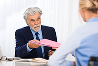 Anwaltskosten und Steuern – was gilt? Ein Anwalt übergibt der Mandantin ihre Rechnung, die sie mit Hilfe des Steuerrings steuerlich absetzen kann.