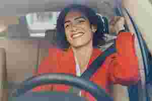 Eine Frau mit rotem Oberteil sitzt lächelnd in ihrem Auto.