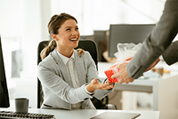 Junger Geschäftsmann überrascht seine Kollegin im Büro mit einem Geschenk.