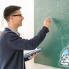 Ein junger Lehrer steht an der Tafel und schreibt Formeln auf.