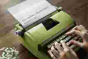 Eine Schreibmaschine ist auf einem Holztisch platziert. Auf der Maschine liegen zwei Hände, die beginnen etwas abzutippen. Auf dem Blatt in der Schreibmaschine erkennt man bereits den Anfang des Schriftsatzes „Ein halbes Jahrhundert Steuerring“. 