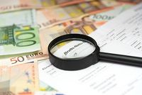 Lohnsteuerabzugsmerkmale prüfen und korrigieren Auf mehreren Geldscheinen liegt der Auszug einer Lohnsteuerbescheinigung. Auf dieser liegt eine Lupe, die die Worte „Brutto-Netto“ vergrößert.