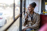 Entfernungspauschale 2025: Fahrtkosten richtig in der Steuererklärung absetzen Eine lächelnde Frau sitzt in einem Bus am Fenster und telefoniert mit einem Smartphone. Dank dem Steuerring weiß sie, dass sie die Fahrkosten steuerlich absetzen kann.