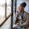 Eine lächelnde Frau sitzt in einem Bus am Fenster und telefoniert mit einem Smartphone. Dank dem Steuerring weiß sie, dass sie die Fahrkosten steuerlich absetzen kann.