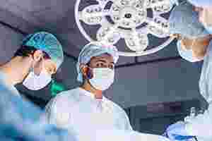 Ein Team aus Ärzten und Pflegern, bestehend aus vier Personen, stehen in OP-Kleidung am Operationstisch und arbeiten konzentriert.