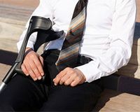 Krankengeld oder Krankentagegeld – werden Steuern fällig? Mann im Anzug und mit Krücken ruht sich auf einer Bank aus.