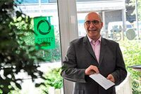 in Mann in Anzug steht vor einer Glastür. Er trägt eine Brille und lächelt. An der Glastür ist das Steuerring-Logo angebracht.