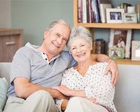 Die Rürup-Rente in der Steuererklärung. Ein älteres Ehepaar sitzt gemeinsam auf der Couch und lächelt in die Kamera.